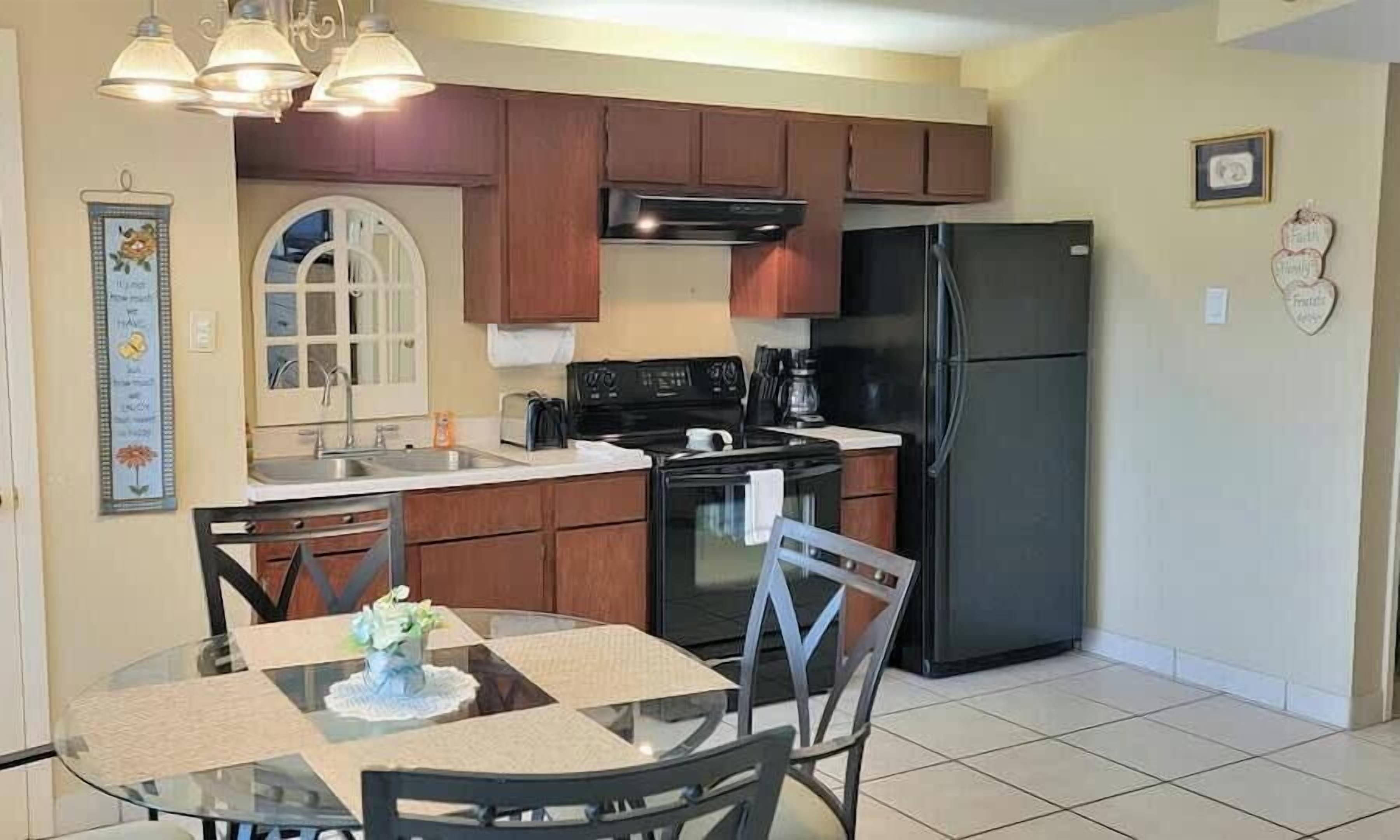 A compact kitchen with wooden cabinets, a black refrigerator, a stove, and a dining table with chairs.
