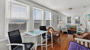 A sunroom with white paneled walls, large windows with blinds, wicker furniture, and a glass-top table. - Oceanfront Getaway - Private Boardwalk, Enclosed sun porch (Folly Beach)