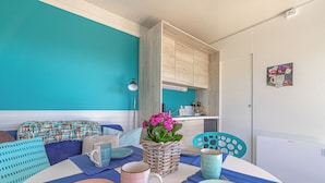 Un coin repas avec une table dressée pour deux personnes, un panier en osier rempli de fleurs et, au fond, une cuisine.