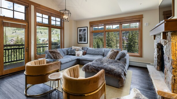 A spacious living room with a large sectional sofa, two rocking chairs, and a stone fireplace.