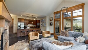 A spacious living area with a gray sofa, a stone fireplace, and a kitchen in the background.