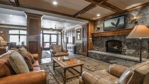 A spacious living room with leather furniture, a stone fireplace, and a large window.