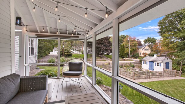 A covered porch with a gray sofa, wicker chair, and string lights. - Family friendly home in heart of Cape Porpoise (Kennebunkport)