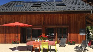 A wooden building with a sloped roof, solar panels, a covered patio with a table and chairs, and potted plants. - 4-room apartment, 8 people, pets allowed, terrace (Valloire)