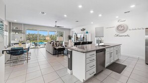 A modern kitchen with a central island, white cabinetry, and a large window overlooking a pool. - Liberty Hope: Private Pool, Water Park, Golf View, Near Disney (Kissimmee)