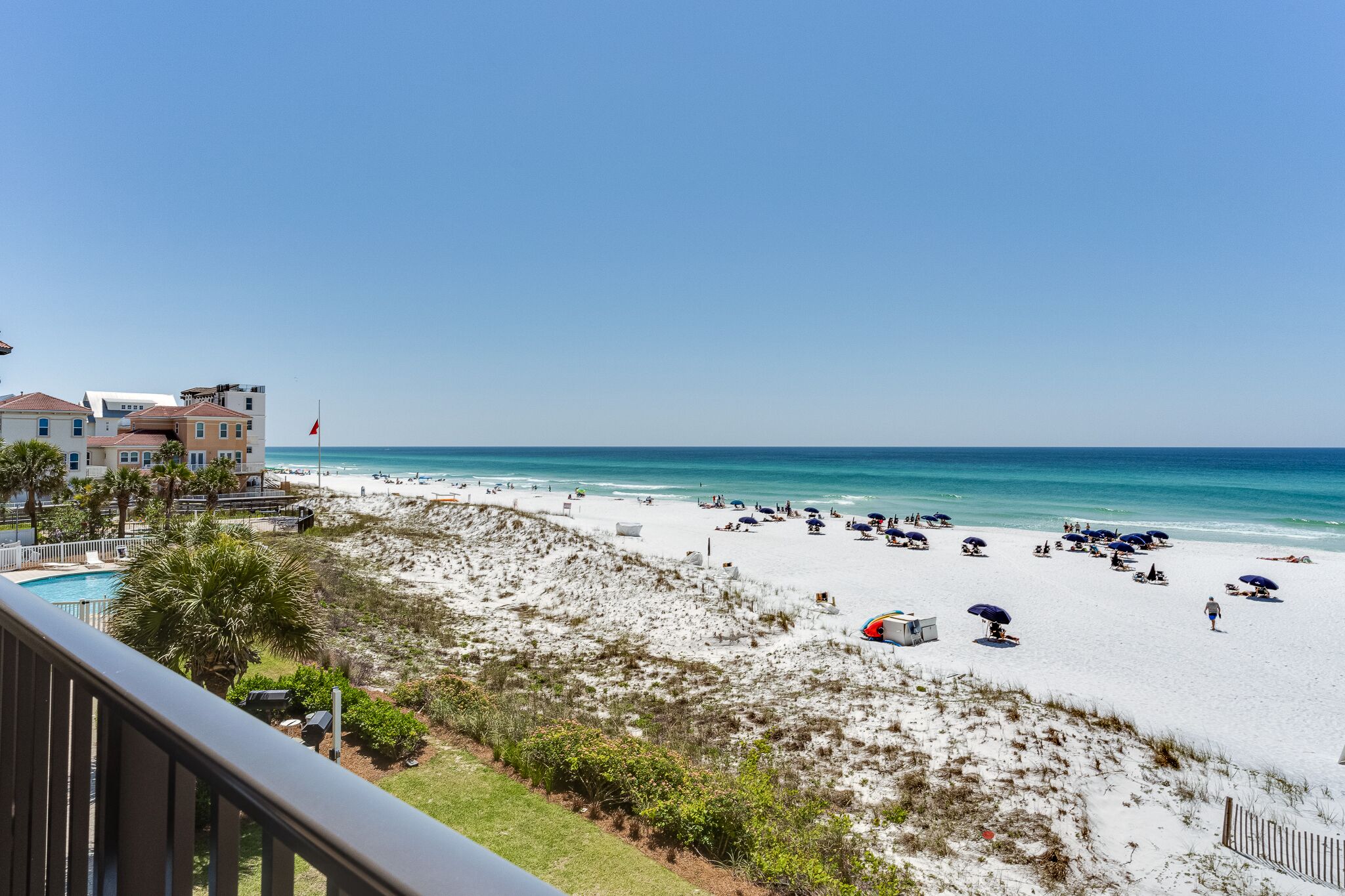 A beach with a pool, beach umbrellas, and a flag.