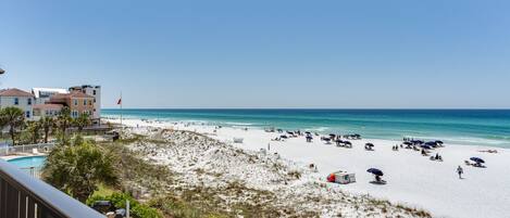 A beach with a pool, beach umbrellas, and a flag.