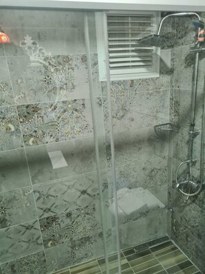 A shower area with a glass door, a showerhead, and a ventilation grille. - Çapari Bozcaada (Bozcaada)