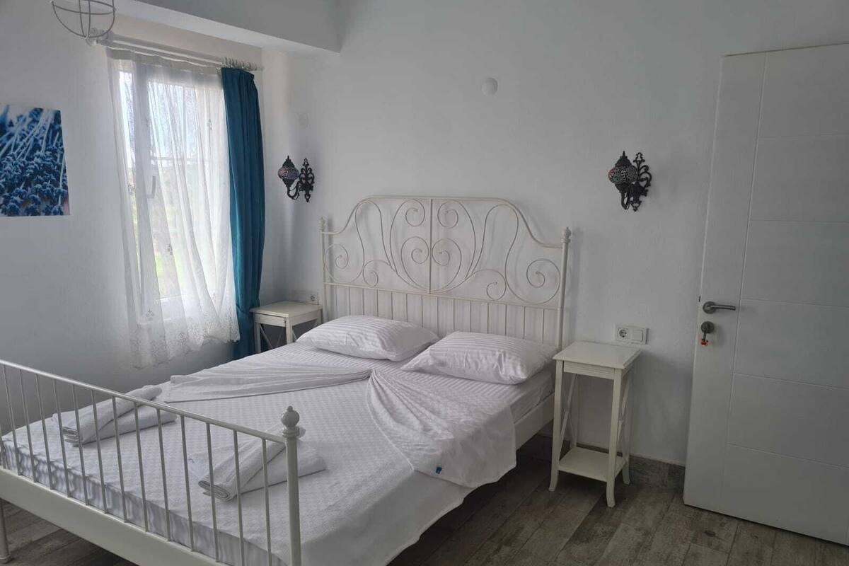 Una cama de metal blanco con dos almohadas, una mesita de noche y una pequeña cómoda.