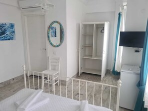A hotel room with a bed, a chair, a wardrobe, a television, and a bathroom with an air conditioning unit. - Çapari Bozcaada (Bozcaada)