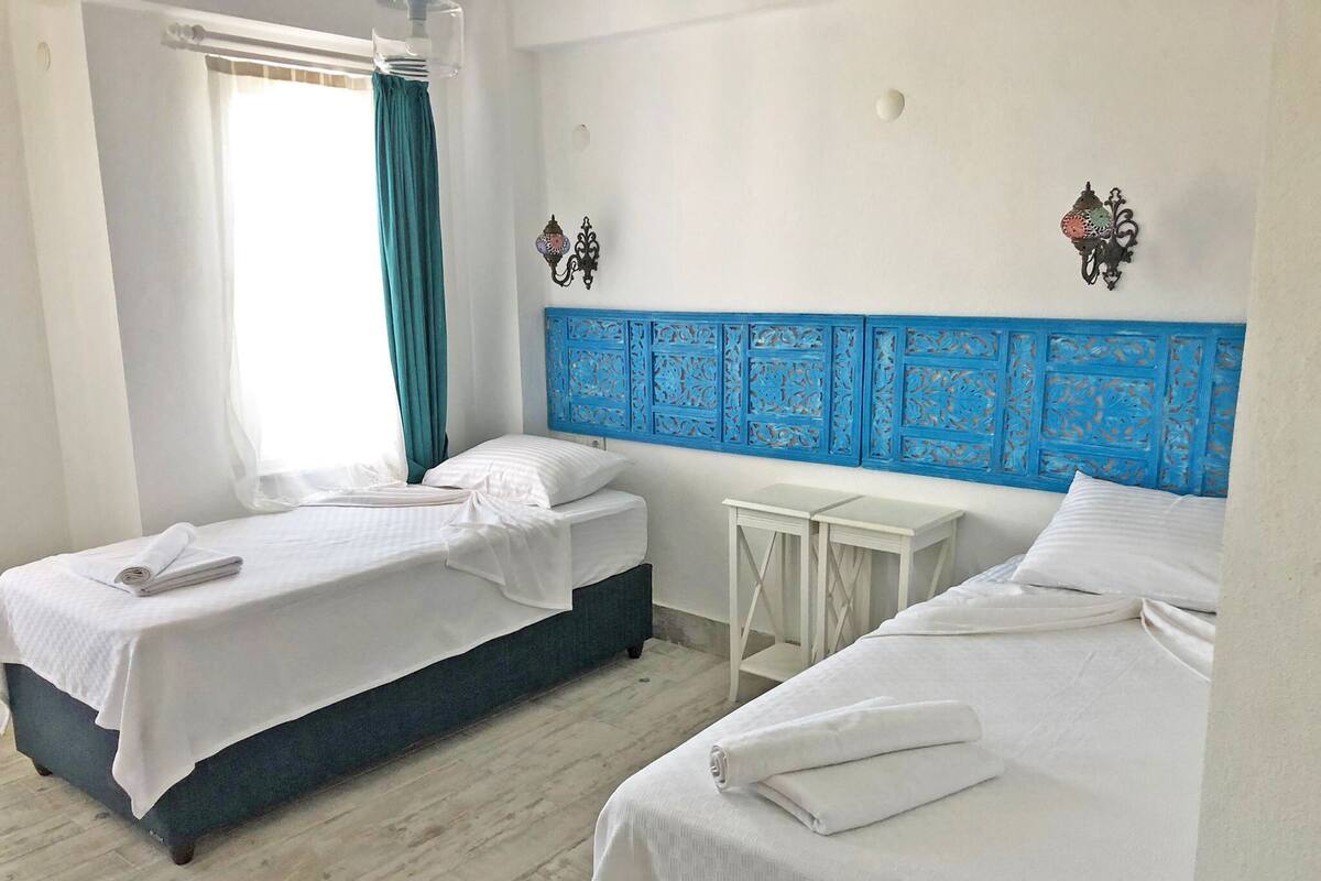 Una habitación de hotel con dos camas, una mesita pequeña blanca y apliques decorativos en la pared.