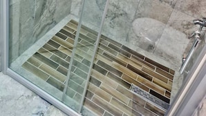 Ducha con paredes de vidrio, suelo de baldosas y desagüe de metal.