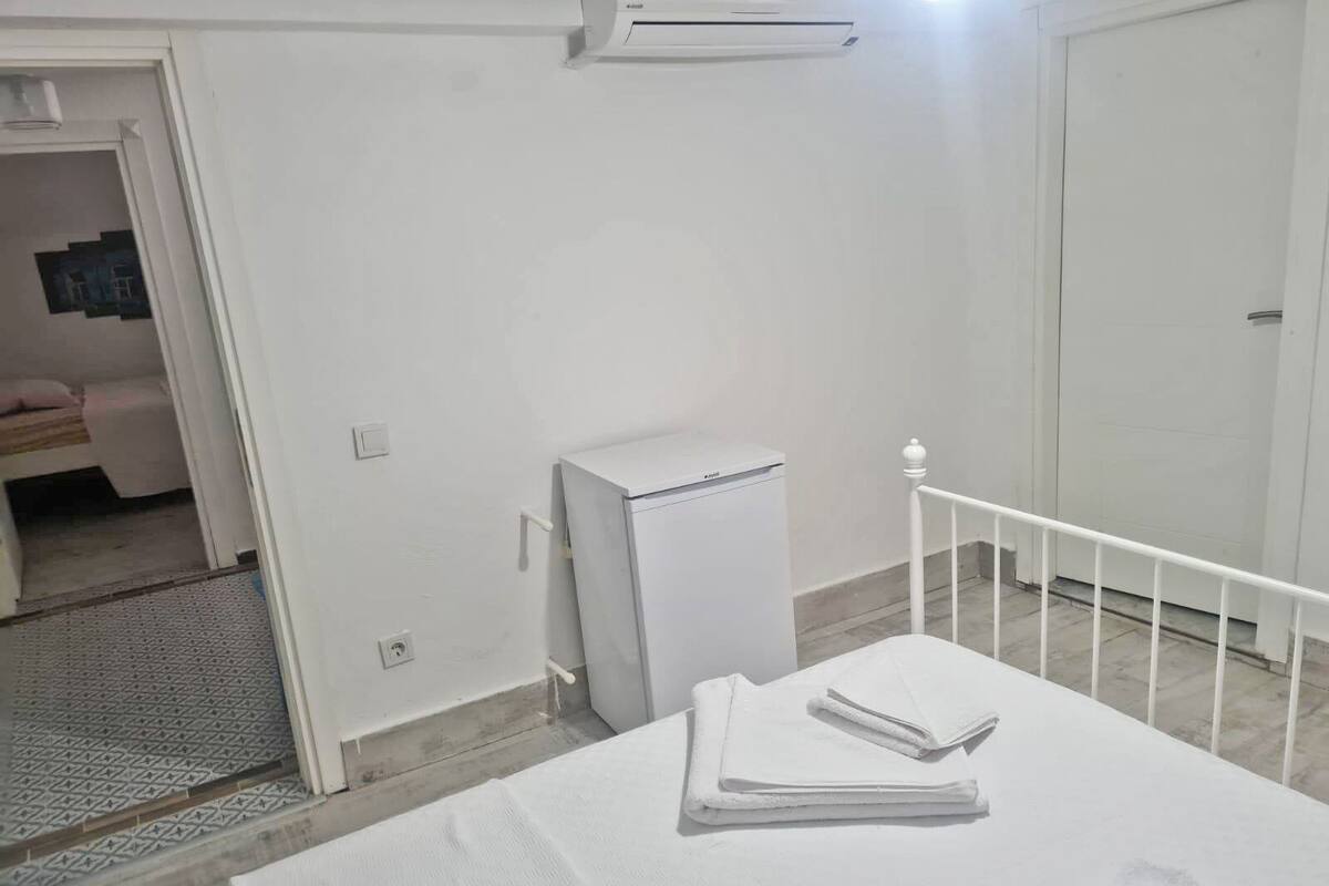 Una habitación con una cama, un armario blanco pequeño y un equipo de aire acondicionado en la pared.
