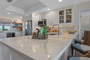 Una cocina moderna con armarios blancos, una isla grande, electrodomésticos de acero inoxidable y sillas de mimbre.