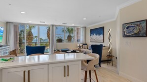 A modern kitchen with a large island, a dining area with a sofa, and a view of palm trees and the sea. - The ONLY 1 Bedroom with a private Bunk Room - Beach Service Included!!! (Miramar Beach)
