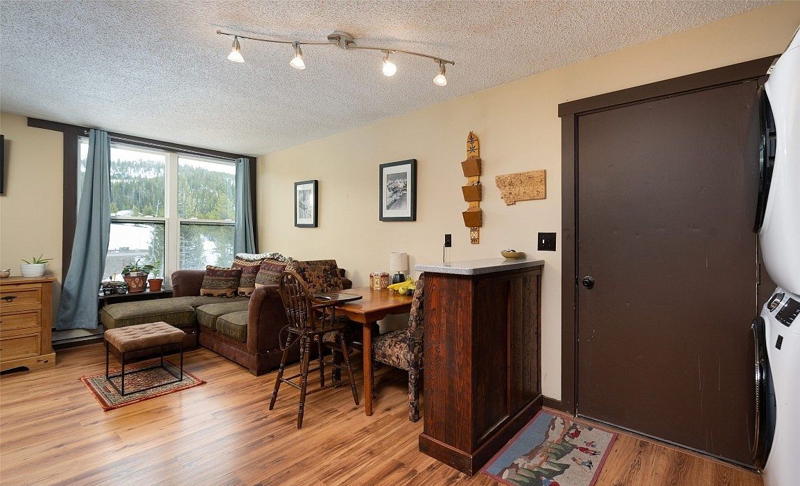 A cozy living room with a sofa, dining table, and chairs, a wooden cabinet, and a large window with curtains.