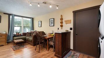 A cozy living room with a sofa, dining table, and chairs, a wooden cabinet, and a large window with curtains.