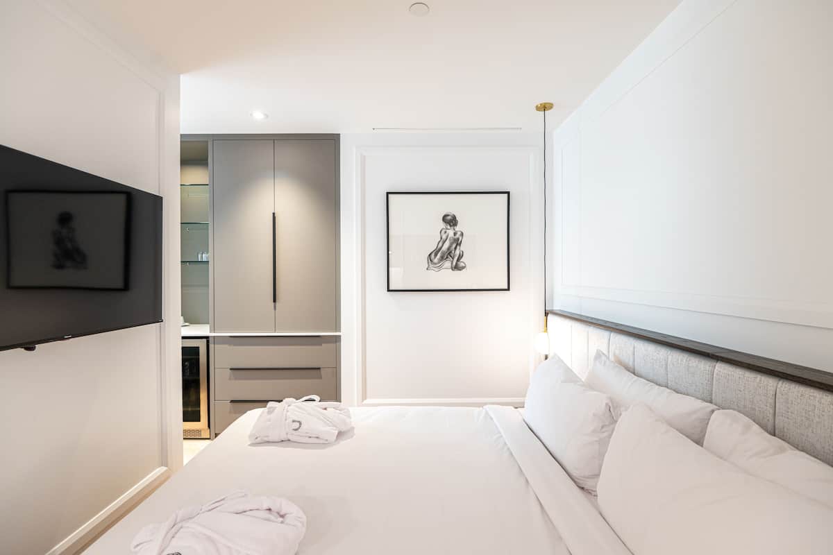 A modern hotel room with a neatly made bed, a robe on the floor, and a framed artwork on the wall.