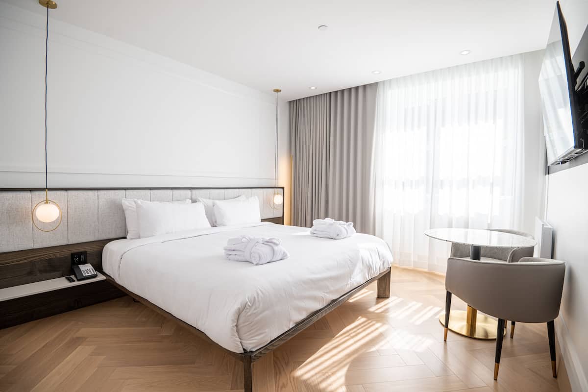 A modern hotel room with a large bed, a bedside table with a phone, a round table, and a TV mounted on the wall.