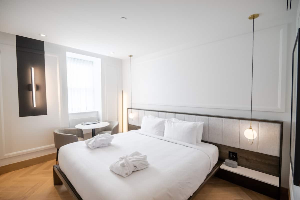 A modern hotel room with a large bed, bedside table, and a small round table.