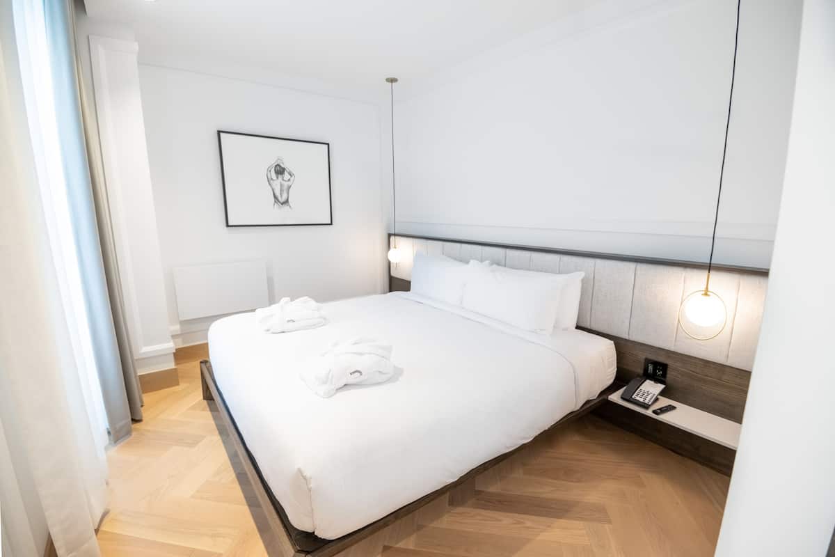 A modern hotel room with a large bed, a bedside table with a phone, and a framed picture on the wall.