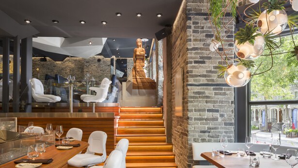 Un restaurante moderno con suelo de madera, sillas de cuero blanco y una pared de ladrillo.