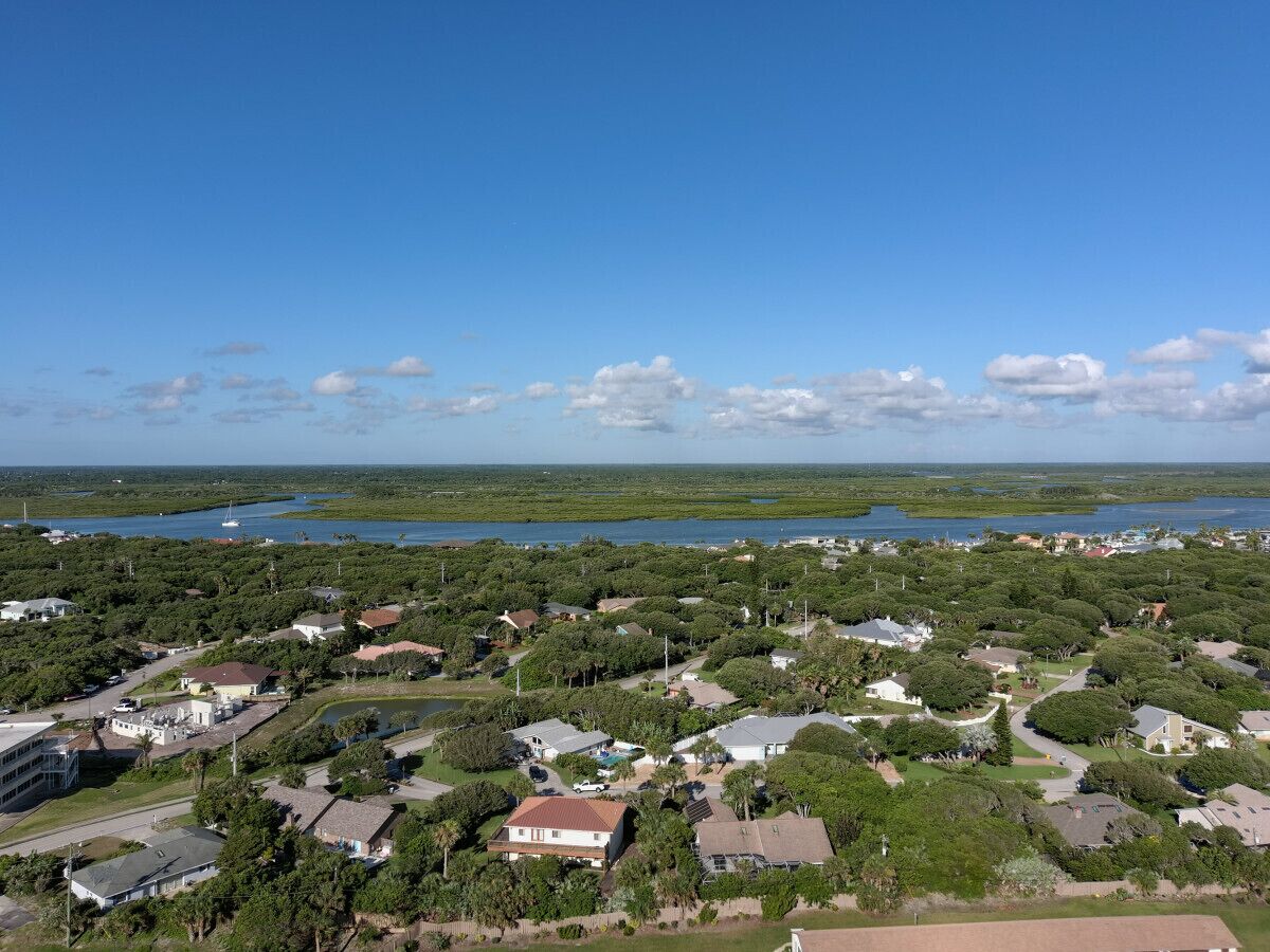 An aerial view of a residential area with houses, roads, and a body of water in the background.