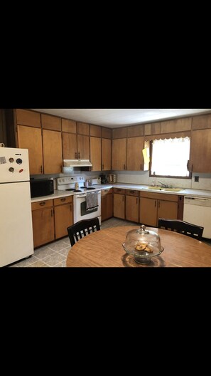 Kitchen features a central island, refrigerator, oven, microwave, and sink, as well as a dining table with chairs.