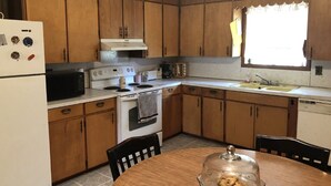 A kitchen with wooden cabinets, a stove, a microwave, a sink, and a dining table with a glass cover.