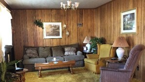 A cozy living room with a wooden paneled wall, a sofa, a coffee table, a chair, and a lamp.
