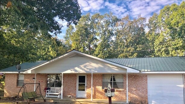 A single-story brick house with a covered porch, a swing set, and a birdhouse.