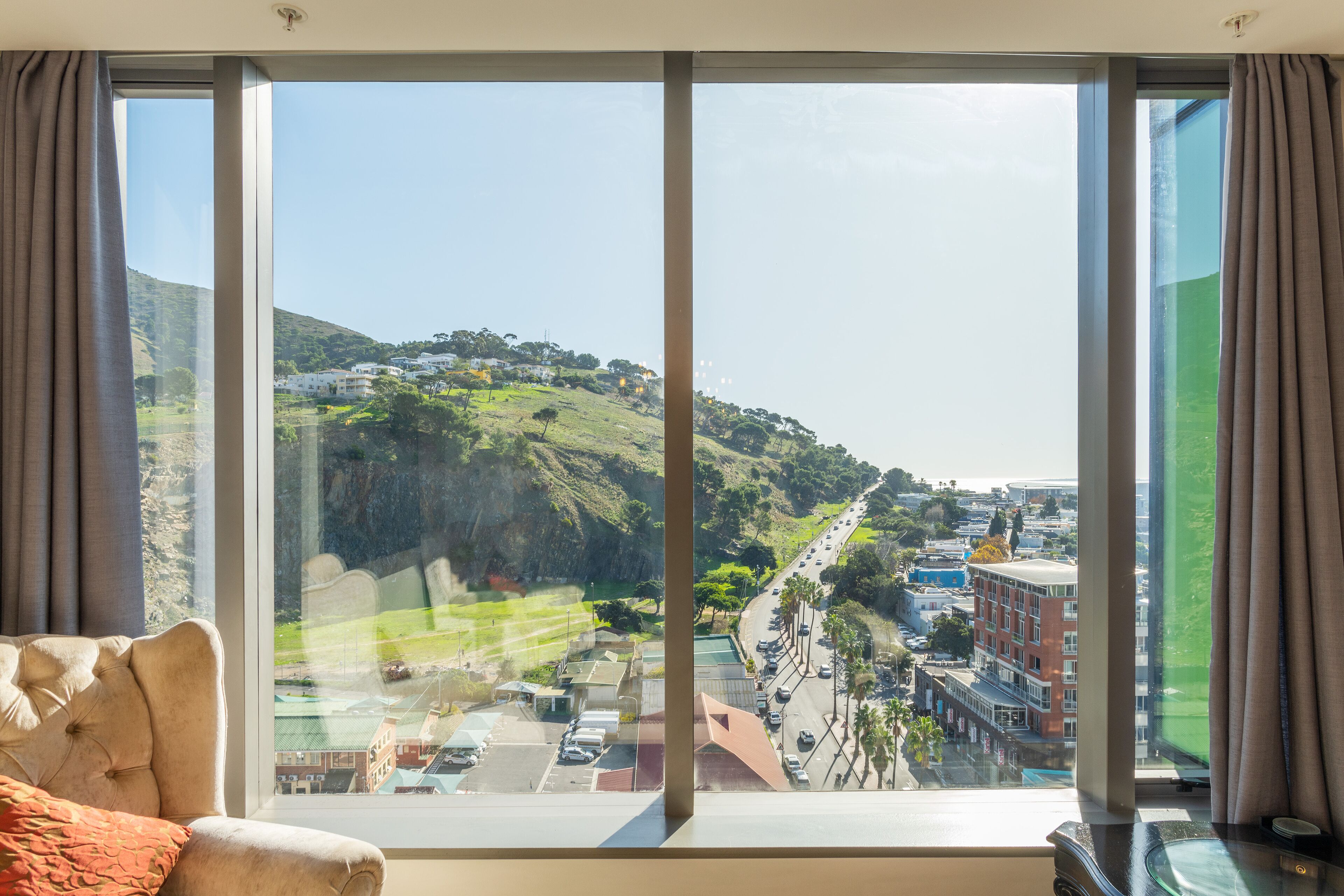 Una habitación con un ventanal grande que ofrece vistas a un paisaje montañoso y una calle con coches estacionados.