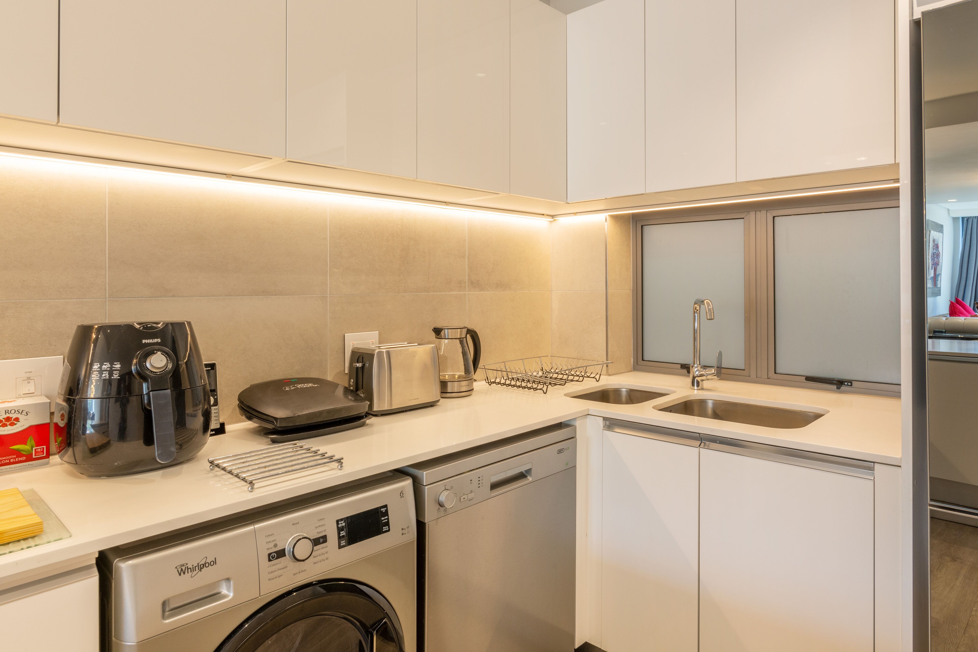 A compact kitchen with a dishwasher, washing machine, toaster, and kettle.