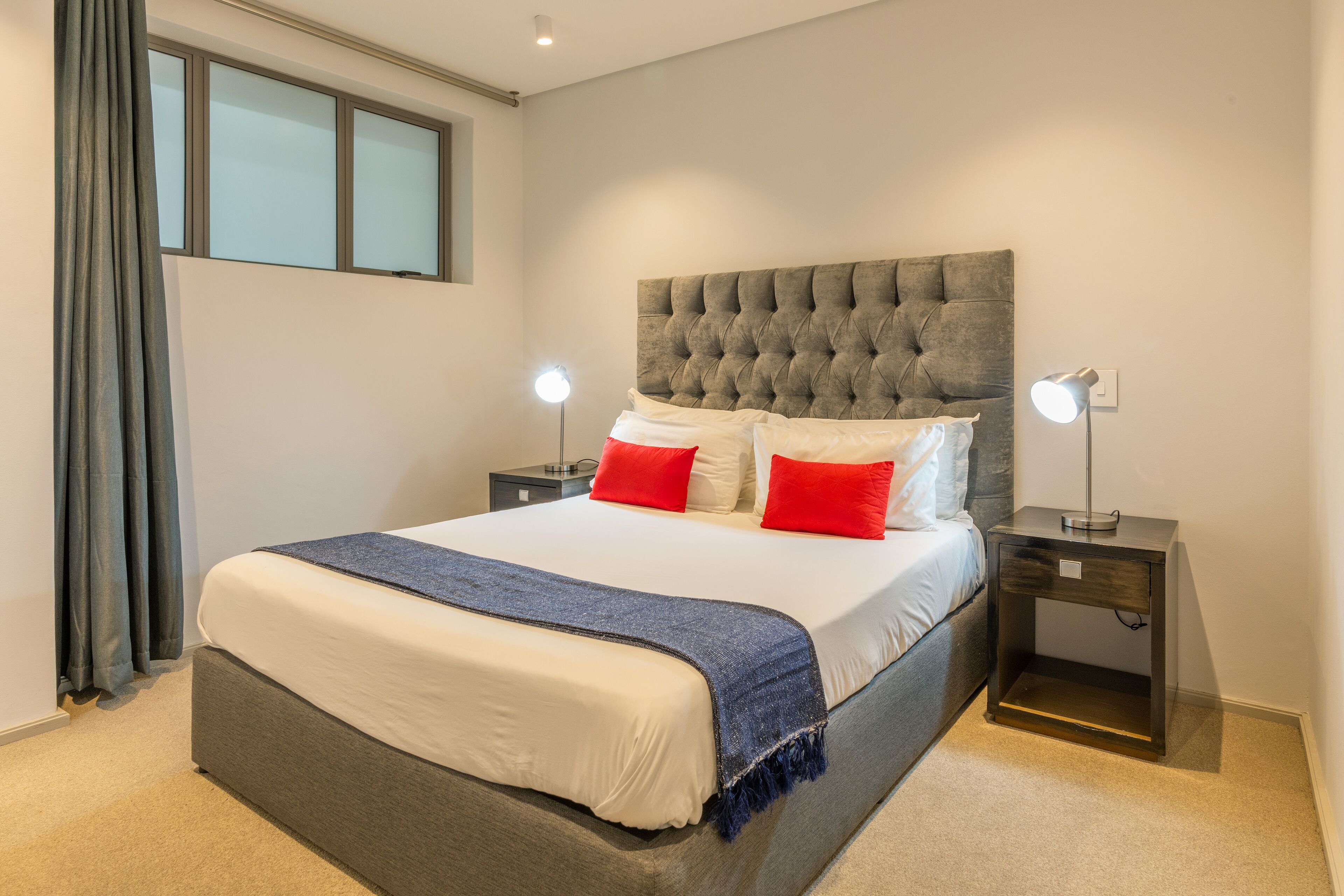 Een slaapkamer met een groot bed, twee nachtkastjes, een raam en een nachtkastje met een lamp.