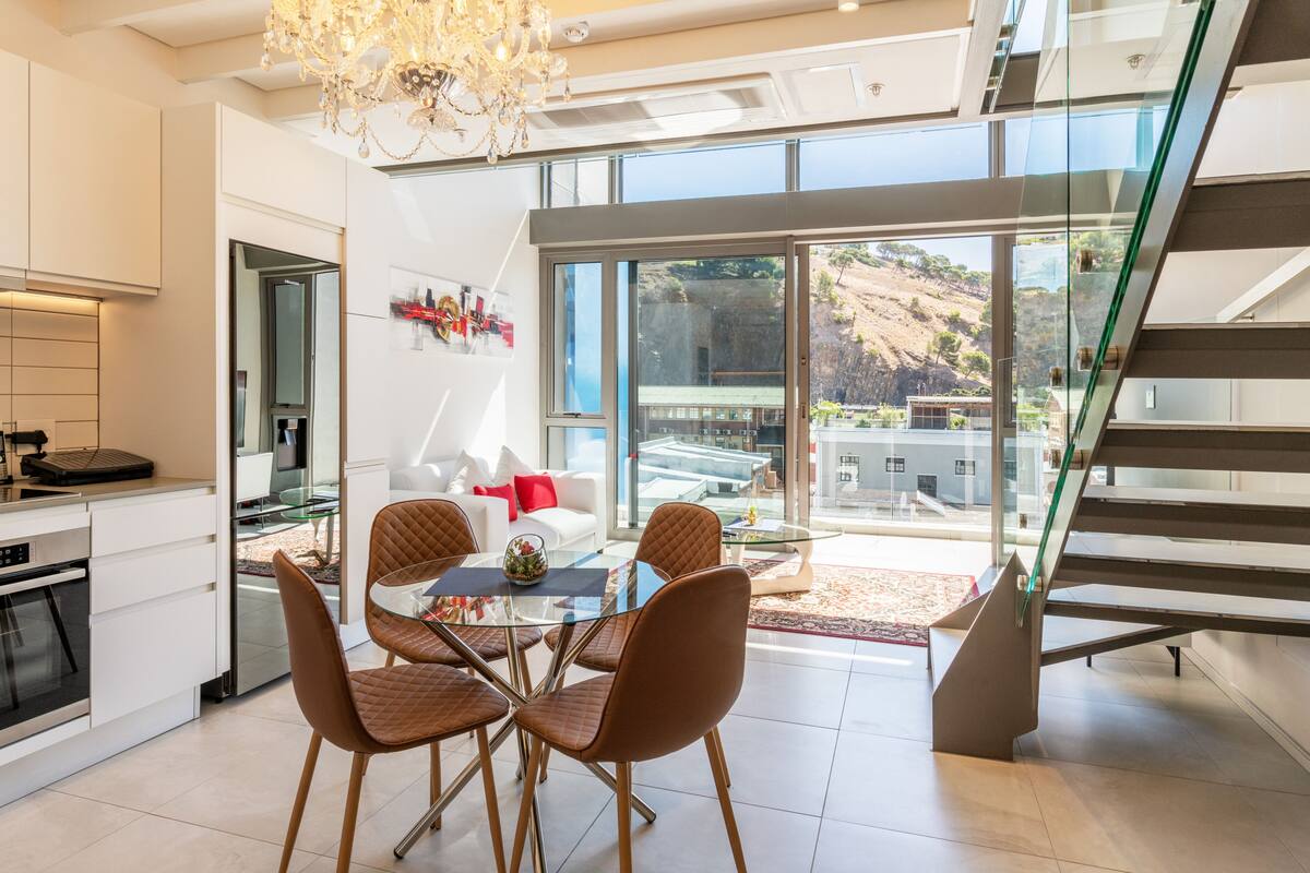 A modern kitchen with a dining area, a staircase, and a view of the outdoors.