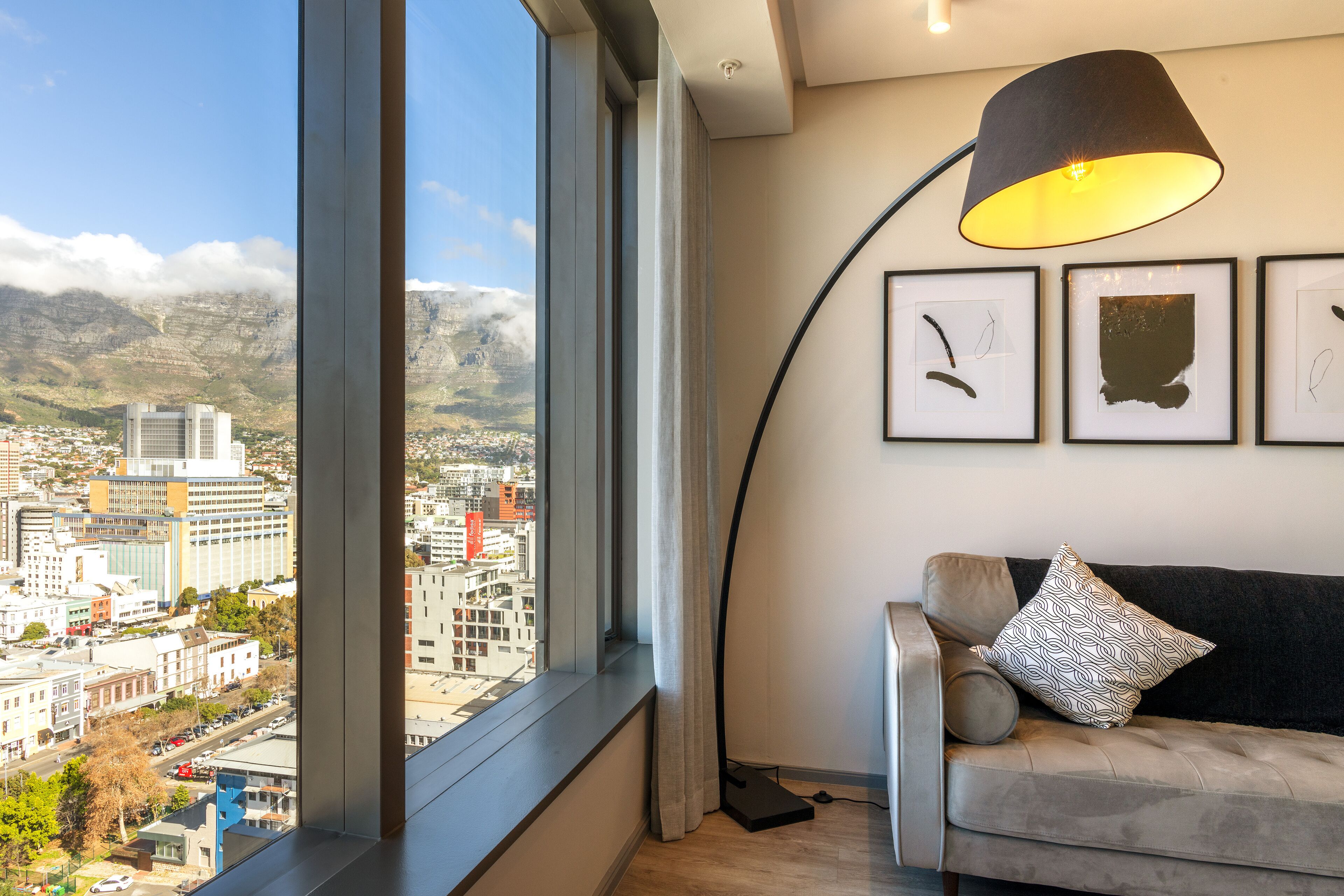 A modern living room with a large window offering a city view, a curved floor lamp, and a sofa with patterned cushions.