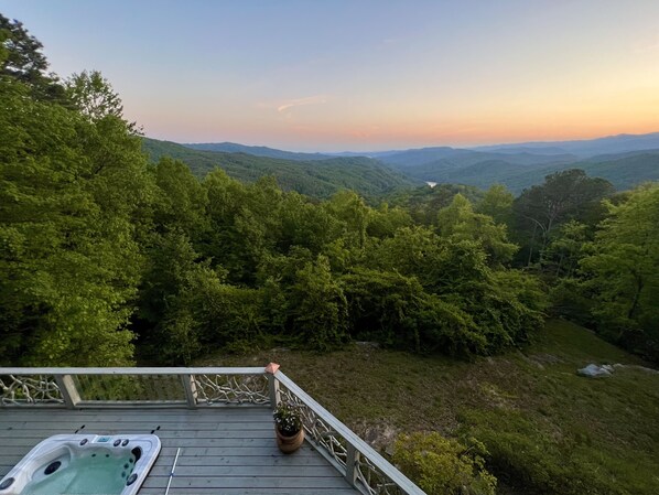 A hot tub on a wooden deck overlooking a forested valley with distant mountains.