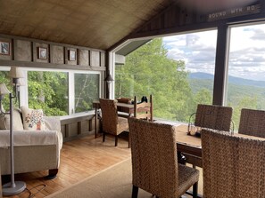 A cozy room with a large window, wicker chairs, a wooden table, and framed pictures on the wall.