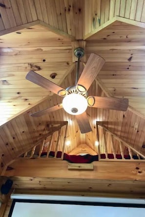 A wooden ceiling with a central fan and a red cushion on a wooden platform.