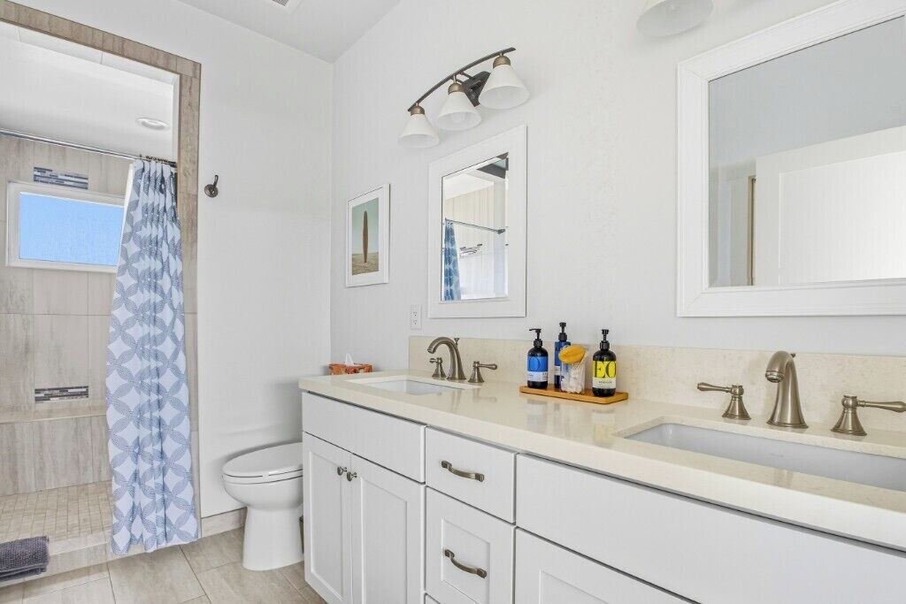 A modern bathroom with a white sink, two faucets, a mirror, and a shower curtain.