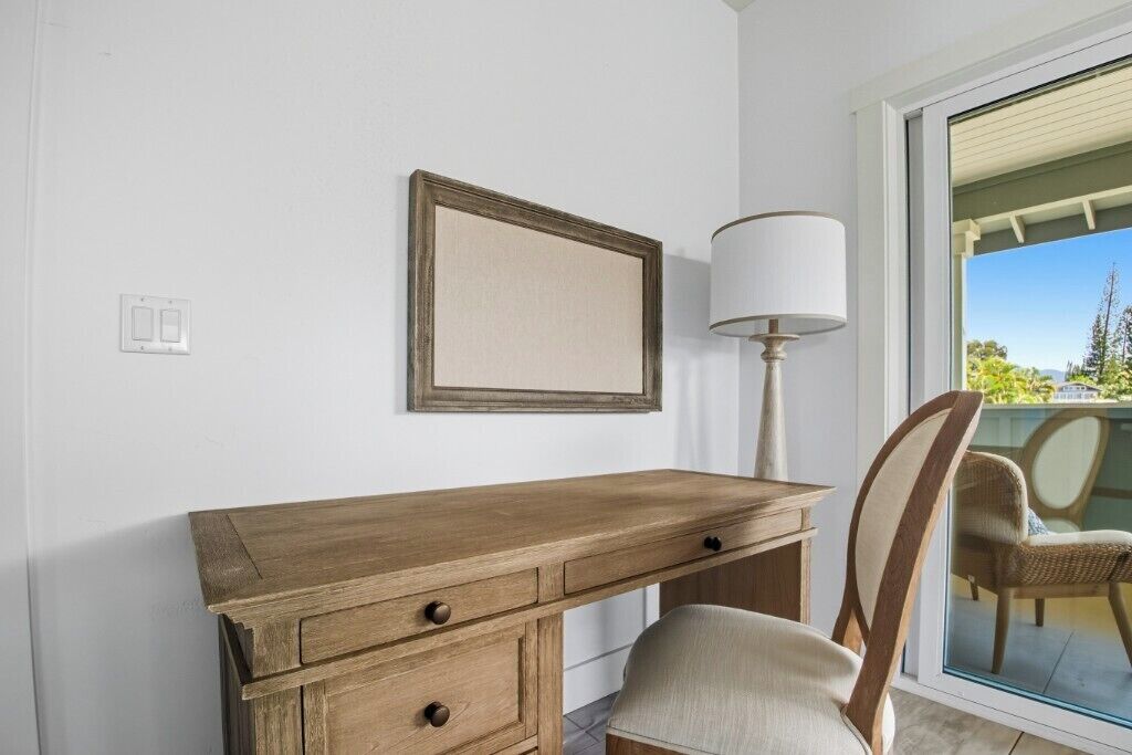 Un bureau en bois avec des tiroirs, une chaise, une lampe et un tableau encadré accroché au mur.