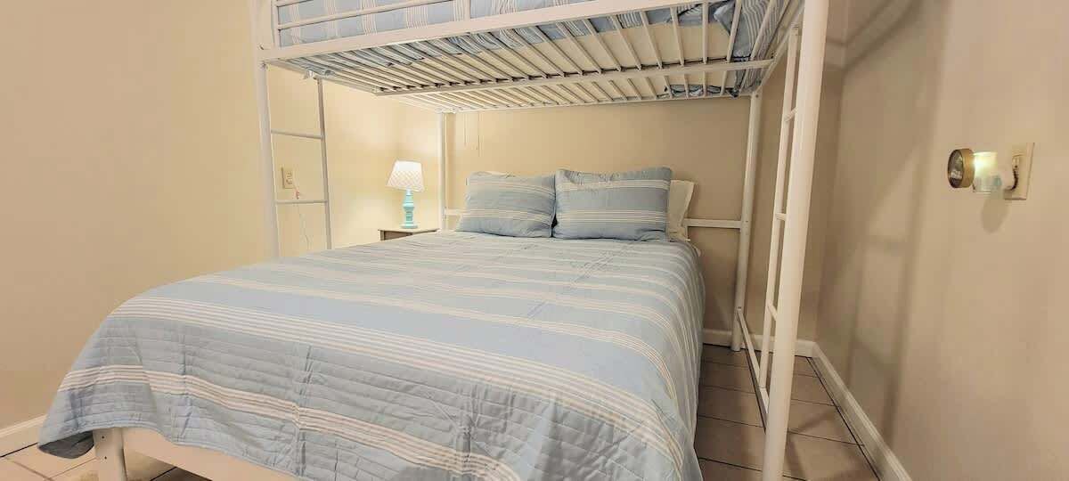 Une chambre avec un lit superposé, une table de chevet avec une lampe et un interrupteur fixé au mur.