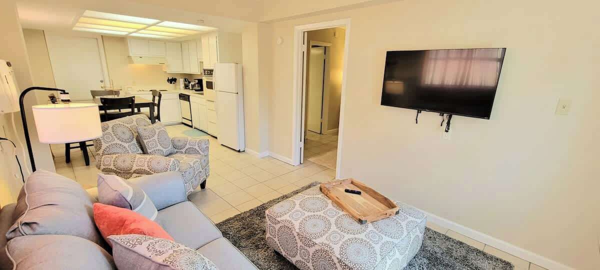 Una sala de estar con sofá, reposapiés y televisor montado en la pared.