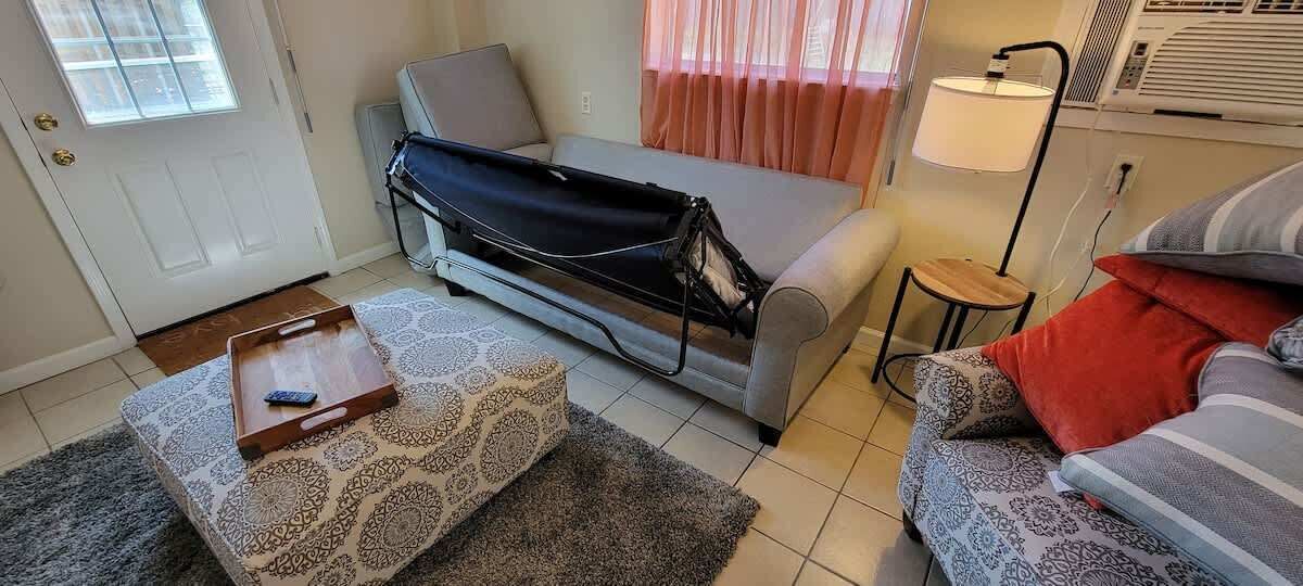 A compact living space with a sofa, a small table with a tray, a patterned rug, and a lamp.