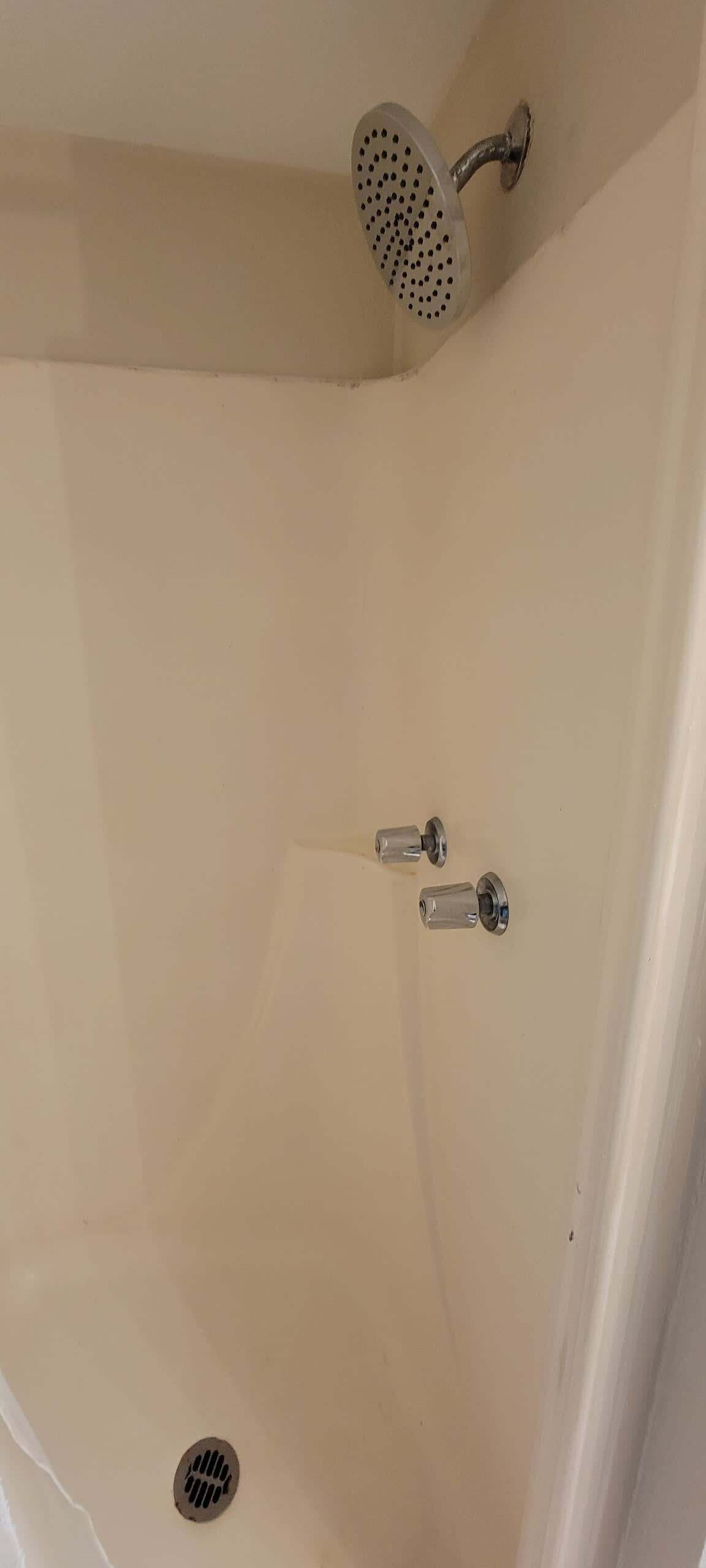 Ein Eckbereich eines Badezimmers mit einer Duschbrause, einem Abfluss und zwei Wasserhähnen.