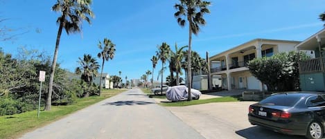 Una calle residencial bordeada de palmeras y casas, un coche cubierto y un coche estacionado.
