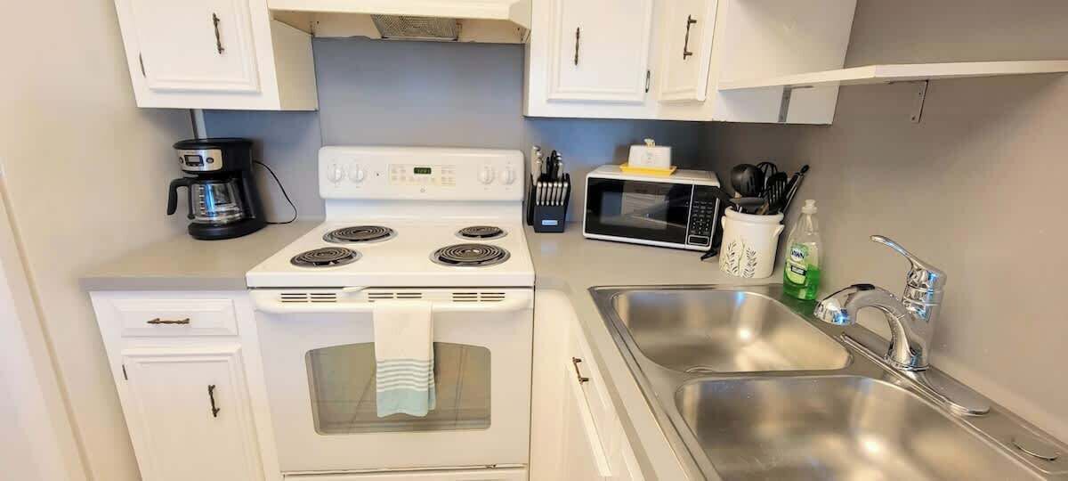 Una cocina compacta con estufa, microondas, pileta y armarios blancos.