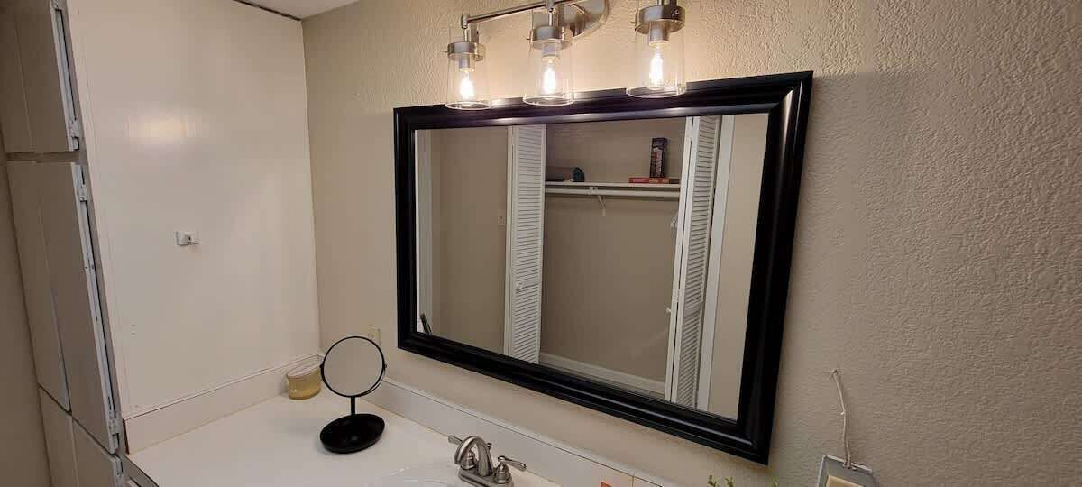 A bathroom with a large mirror, a sink, and a towel rack.