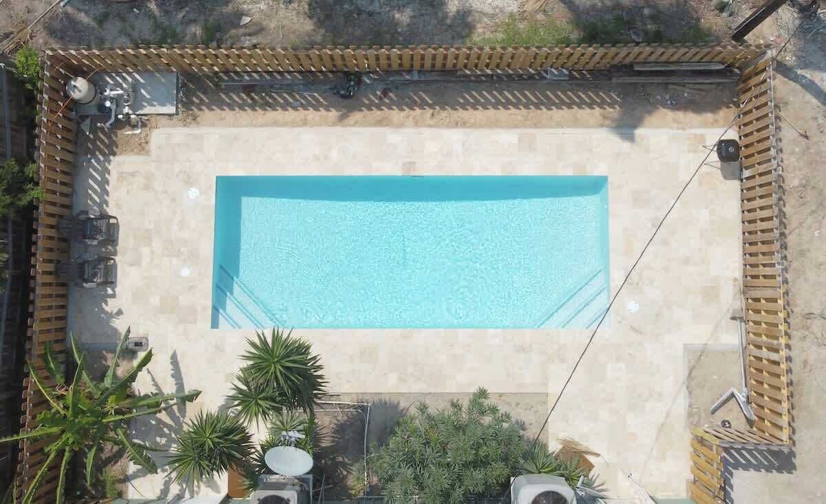 A rectangular swimming pool with a tiled deck, surrounded by a wooden fence, and potted plants at the corners.