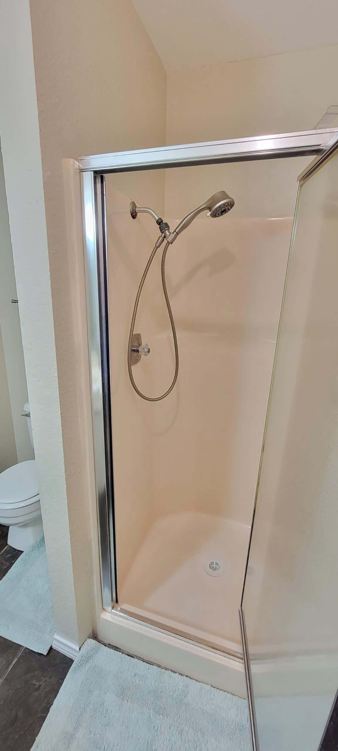 A glass-enclosed shower with a handheld showerhead and a wall-mounted faucet.
